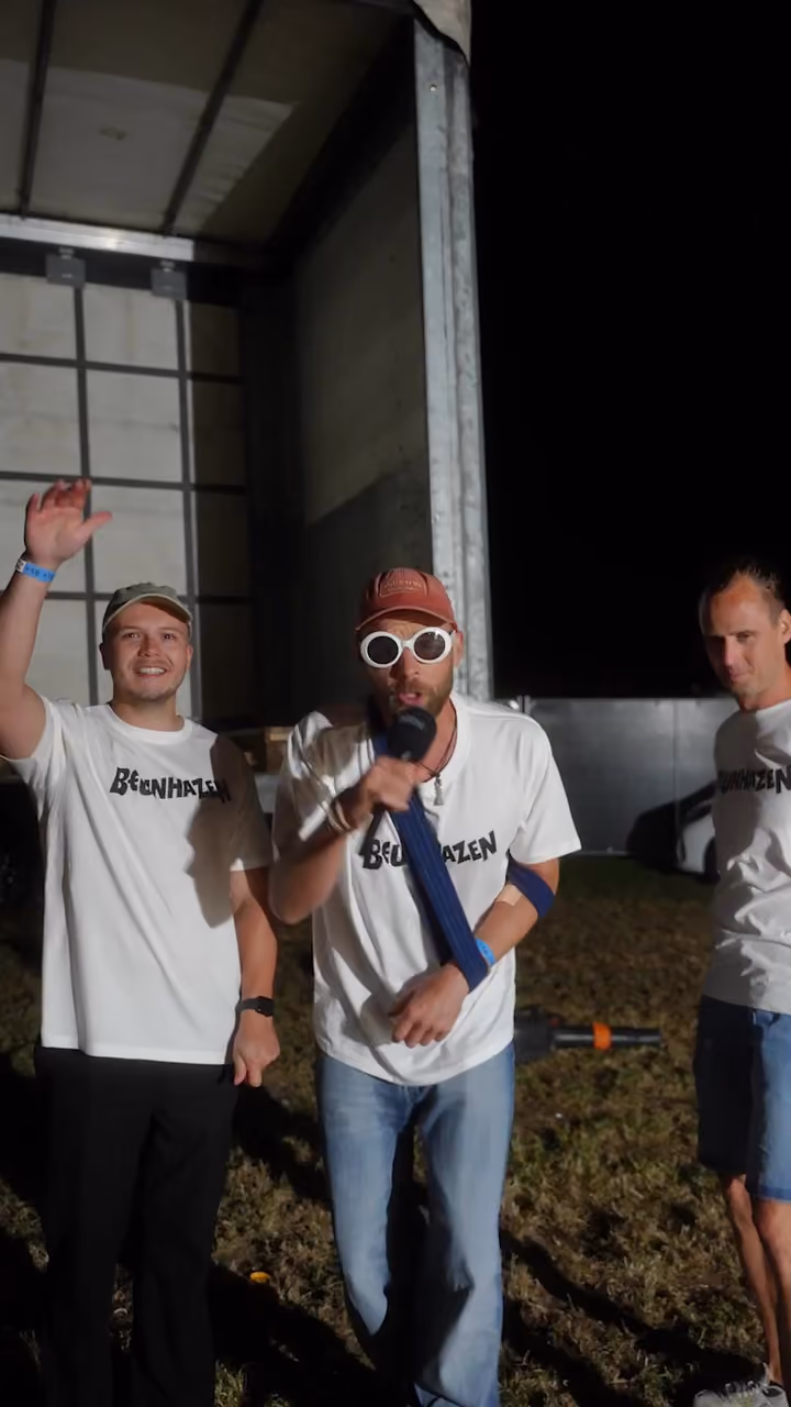 Drie mannen in Beunhazen-shirts bij een vrachtwagen, een met microfoon