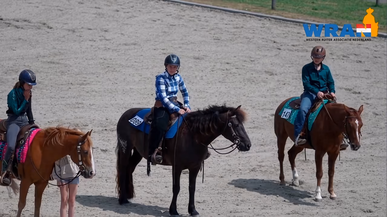 Drie western-ruiters te paard in de zandbak tijdens het NK